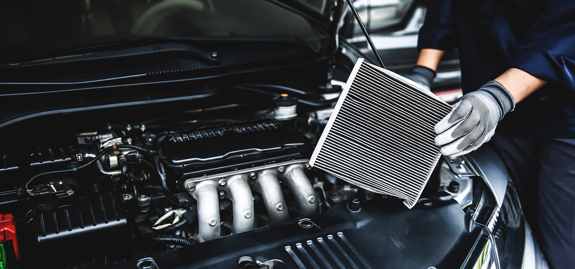 A Telle Tire mechanic holding an air filter on a vehicle engine during AC service.