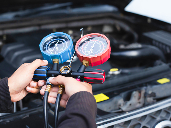 A Telle Tire mechanic using an AC mainfold gauge set to check and service a vehicle's air conditioning system.