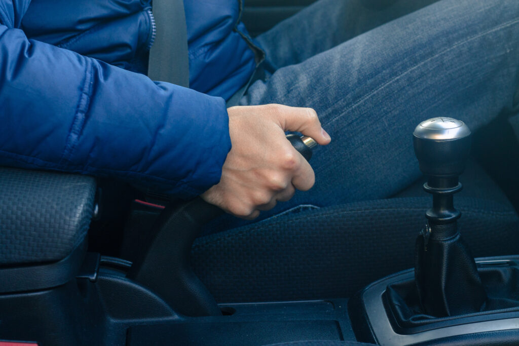 Closeup of a persons hands pulling an emergency brake on a non descript car