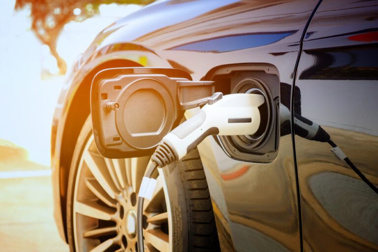 Close up of an EV vehicle charging up, with front driver's side tire showing just behind the charging cable.