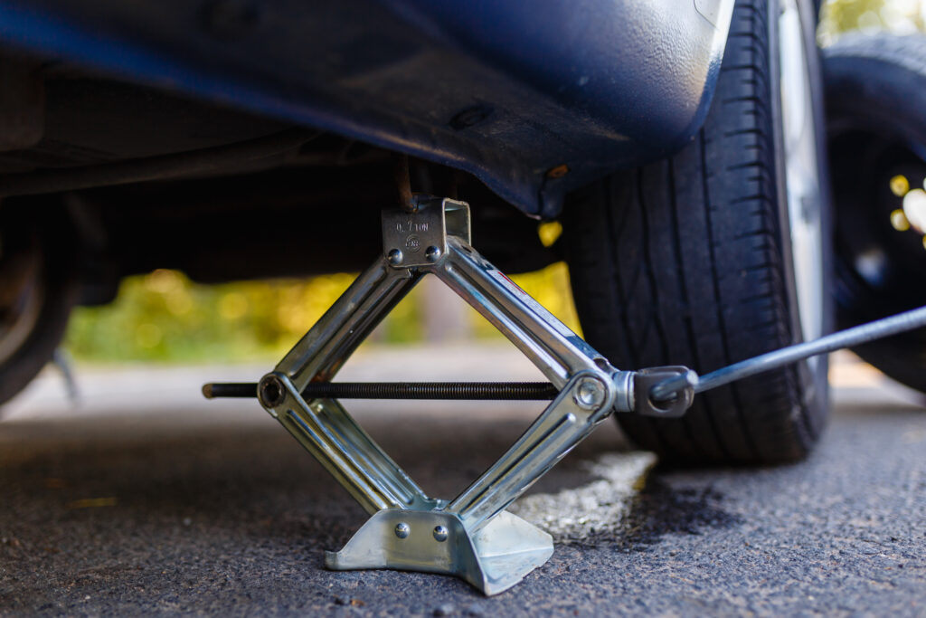 Closeup of a car jack that has a car raised slightly off of some pavement