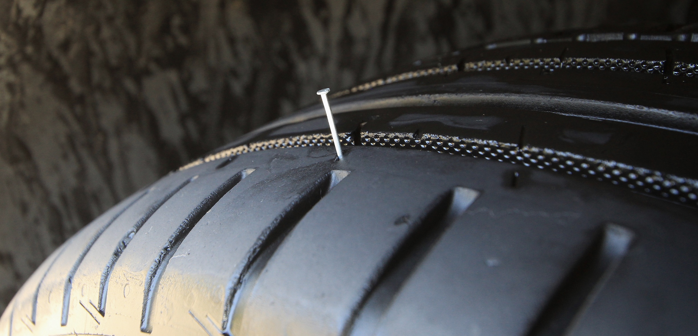 Close up of a run-flat tire with a metal nail sticking out from the tread.