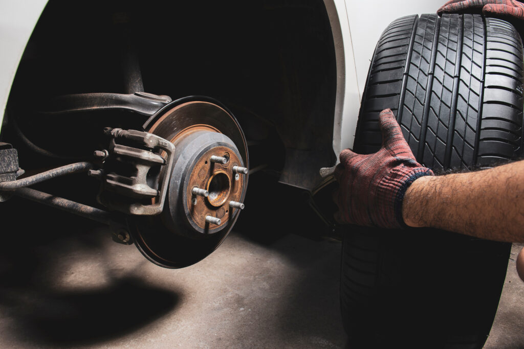 Closeup of gloved hands holding a tire next to a wheel well that has no wheel on it