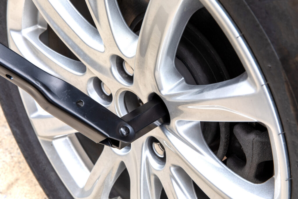 Closeup of a foldable wrench twisting a lug nut on a wheel on a car