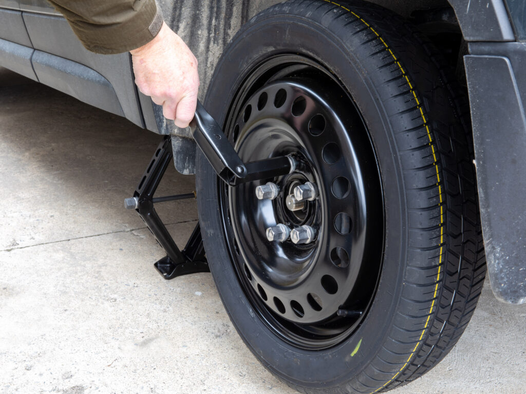Close up of a hand using a foldable wrench to tighten lug nuts of spare tire on a car that is sitting on a jack