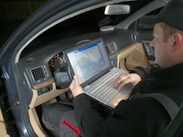 Man in driver's seat conducting diagnostic test on laptop.