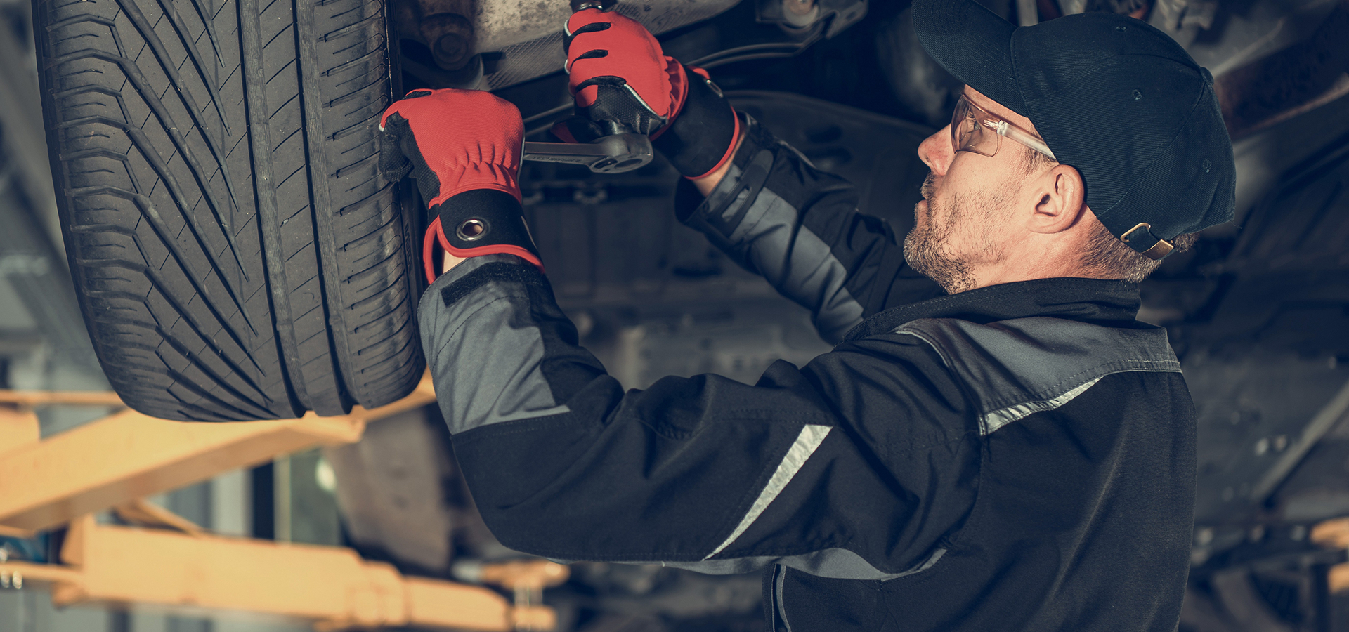 A Telle Tire technician working with a wrench behind the tire under a vehicle that has been elevated on a lift in the shop.