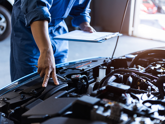 A Telle Tire mechanic, holding a clipboard for repair notes as he examines a vehicle engine.