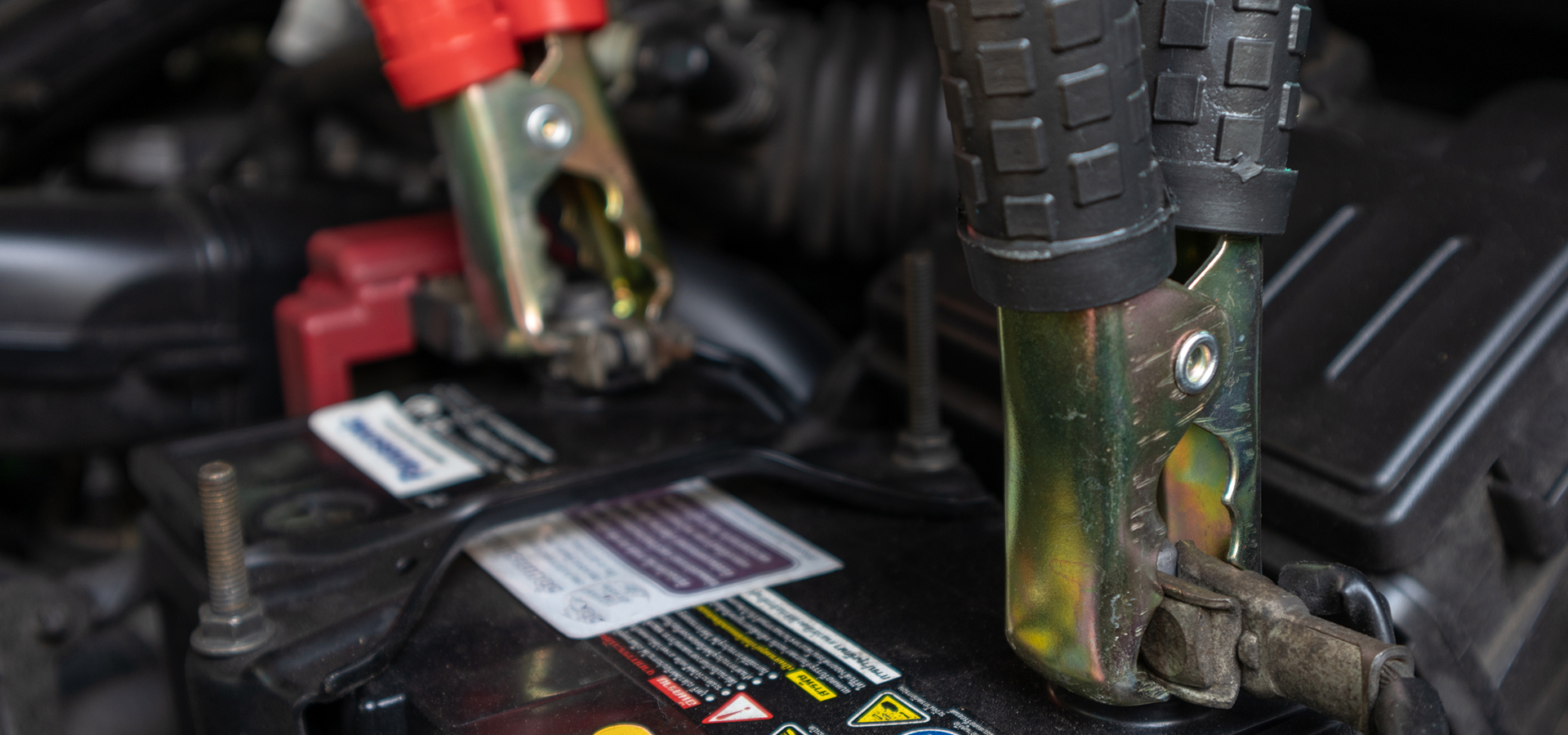 Closeup of a car battery with jumper cables attached during a battery maintenance service.