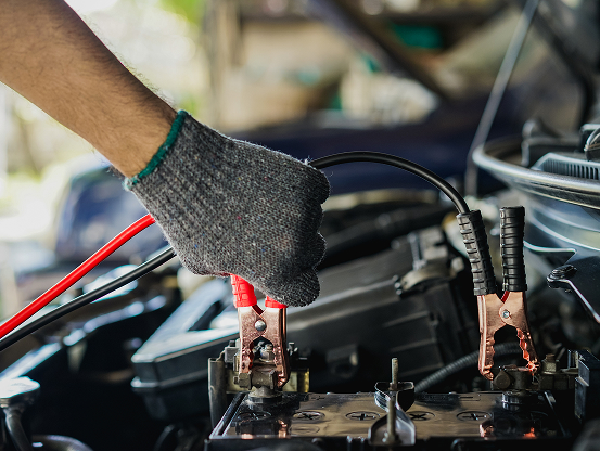 A Telle Tire mechanic's gloved hand connecting cable clamps to a vehicle's battery.
