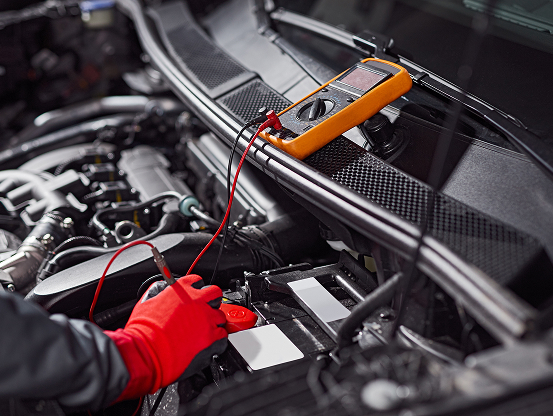 A Telle Tire mechanic's gloved hand using a multimeter to test a car's battery.