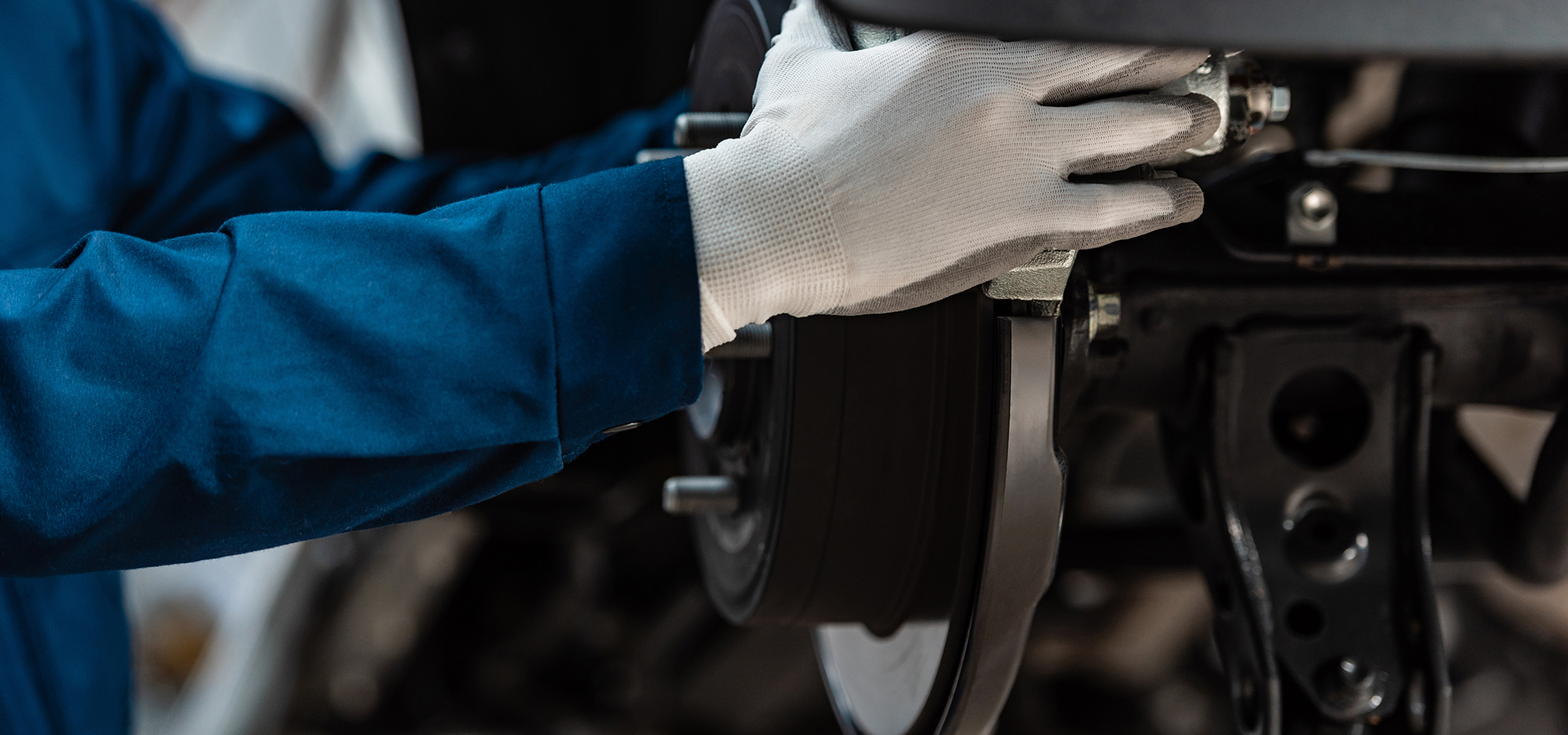 A Telle Tire technician, wearing white work gloves, working to repair the brakes on a vehicle.