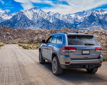 An SUV driving on a rugged dirt road toward snow-covered mountains.