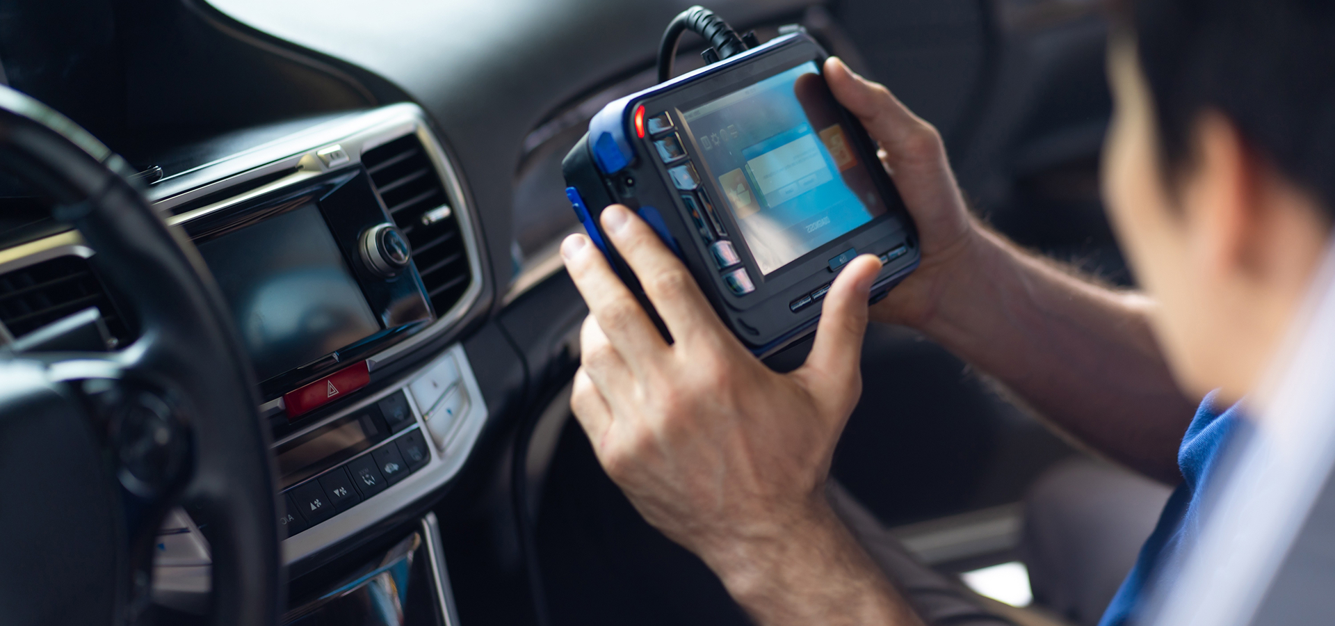 A Telle Tire technician sitting inside a vehicle using a car diagnostic tool connected to the onboard computer system.
