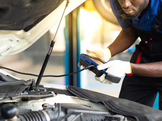 A Telle Tire technician using a computerized car diagnostic tool on a vehicle, connected to the onboard computer system.