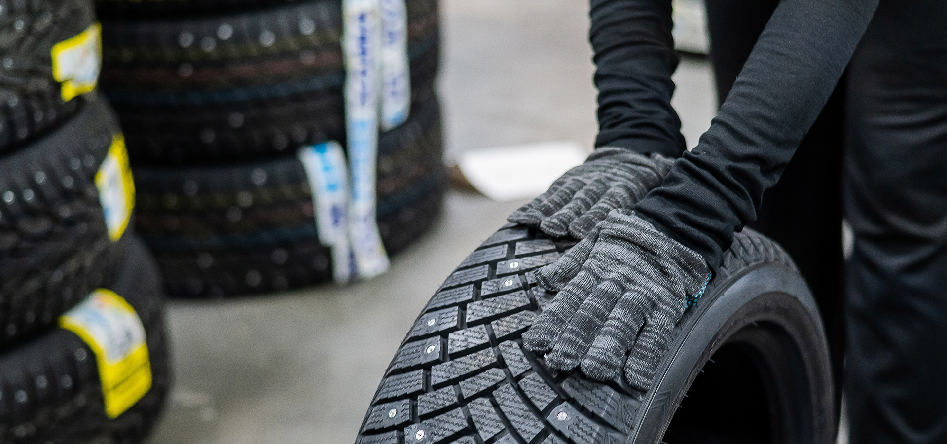 A Telle Tire technician wearing gloves and rolling a new, studded winter tire across the shop.