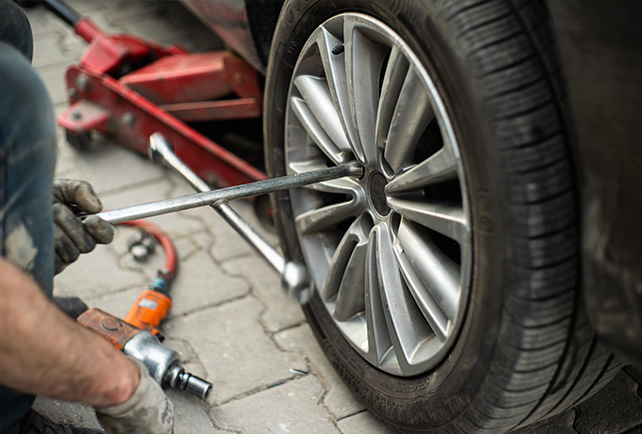 A Telle Tire technician changing a car tire, using a manual wrench to loosen the lug nuts.