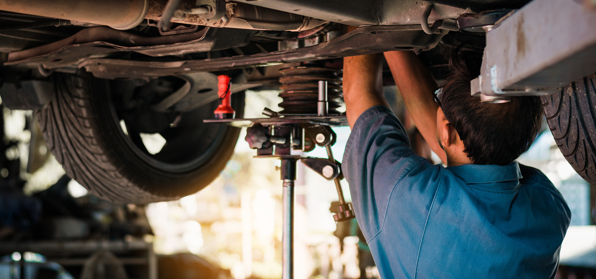 A Telle Tire technician standing and working on the drivetrain beneath a lifted vehicle.