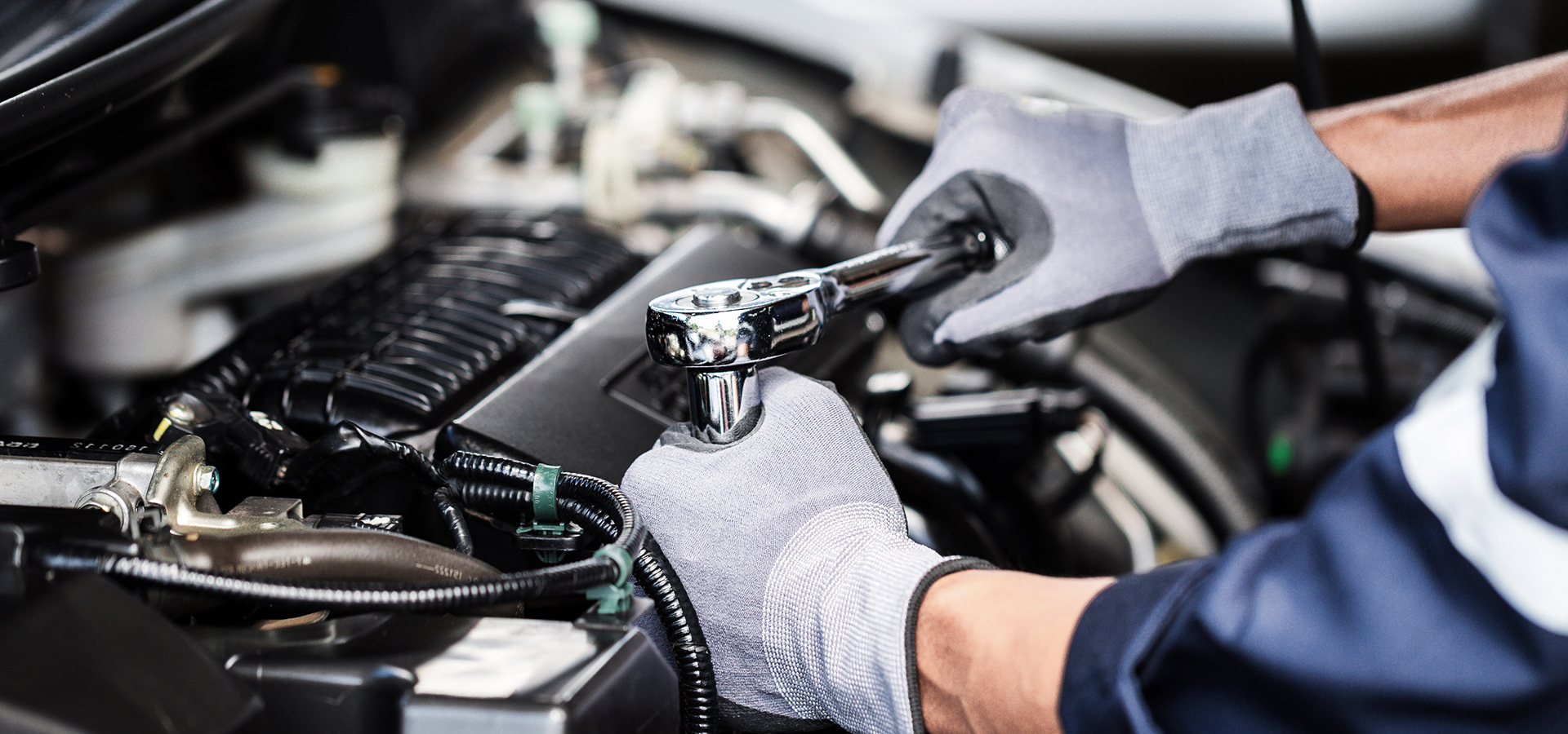 A Telle Tire mechanic using a wrench while working on an engine component during routine automotive maintenance.