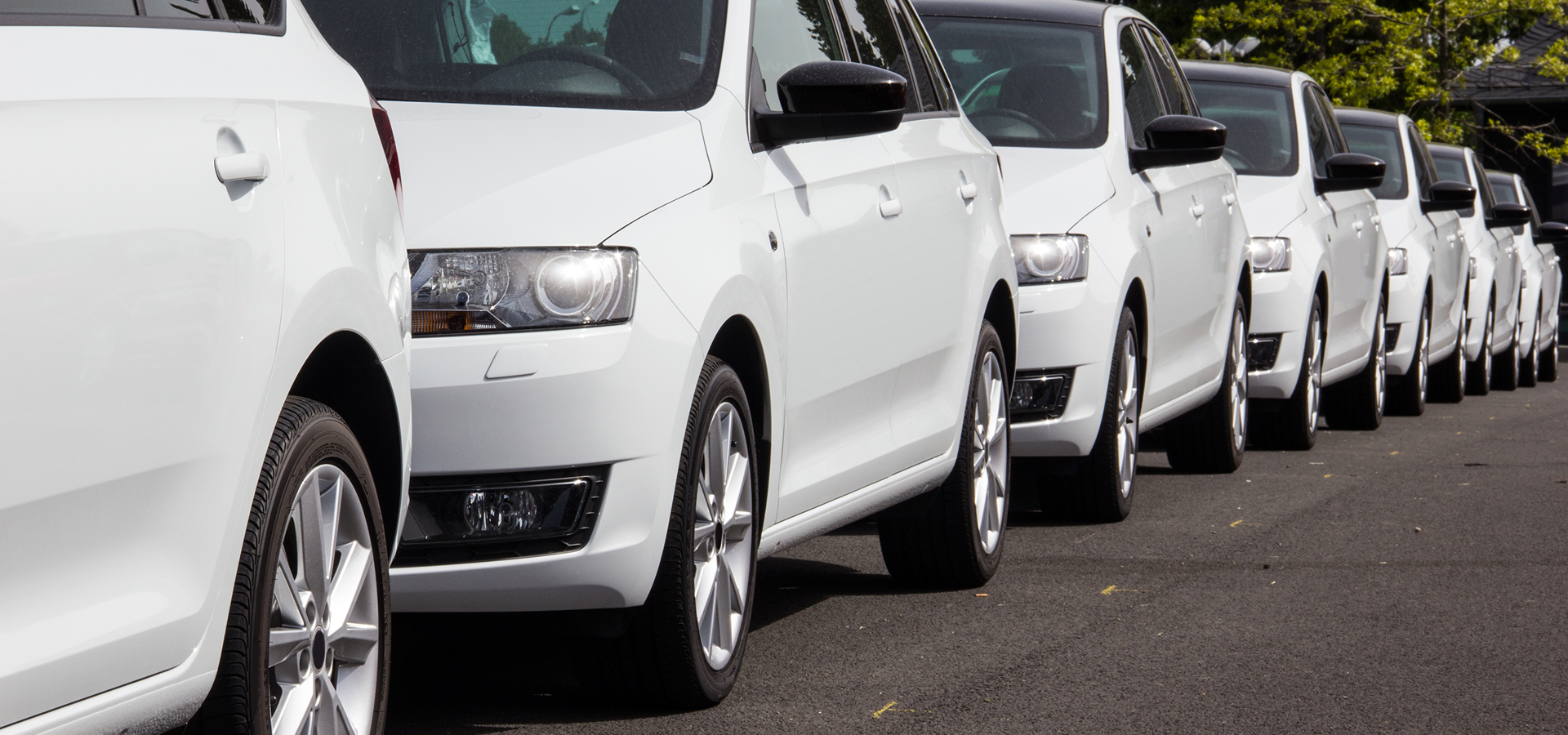 Several matching white commercial vehicles, parallel parked along a roadside.