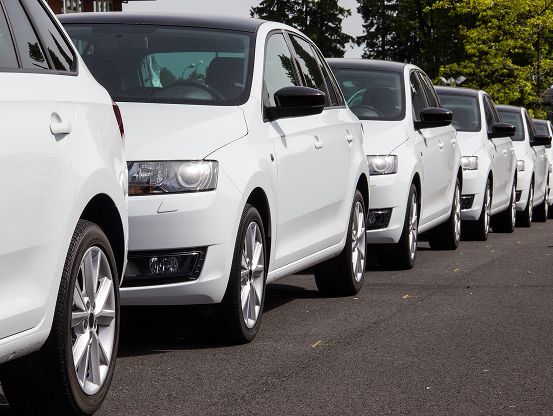 Several matching white commercial vehicles, parallel parked along a roadside.