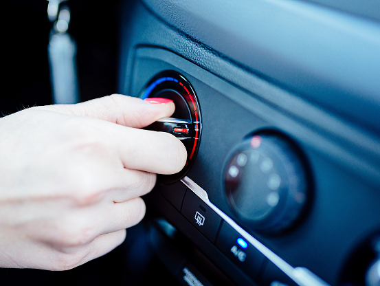 A woman's hand, turning the temperature knob toward high heat on her vehicle's control panel.