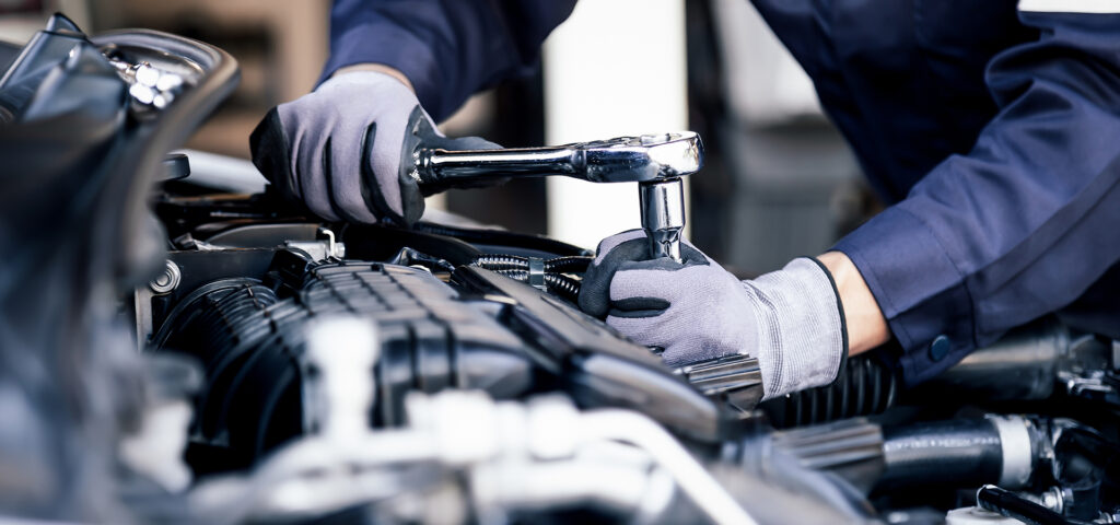 A Telle Tire mechanic using a wrench while working on an engine component during routine automotive maintenance.