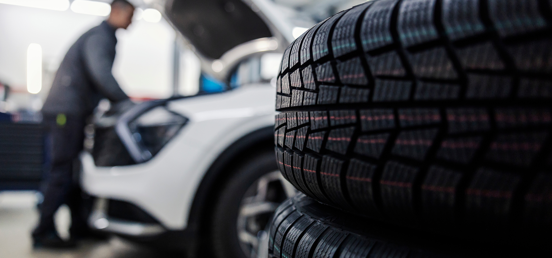 A stack of tires in the foreground with a Telle Tire mechanic working under the hood of a vehicle in the background.