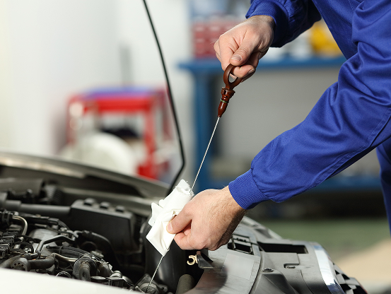 A Telle Tire technician checking the oil level using the dipstick in a vehicle engine.