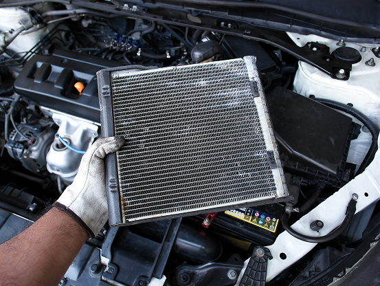 Telle Tire mechanic holding a dirty air filter above a car engine during radiator & cooling system maintenance.