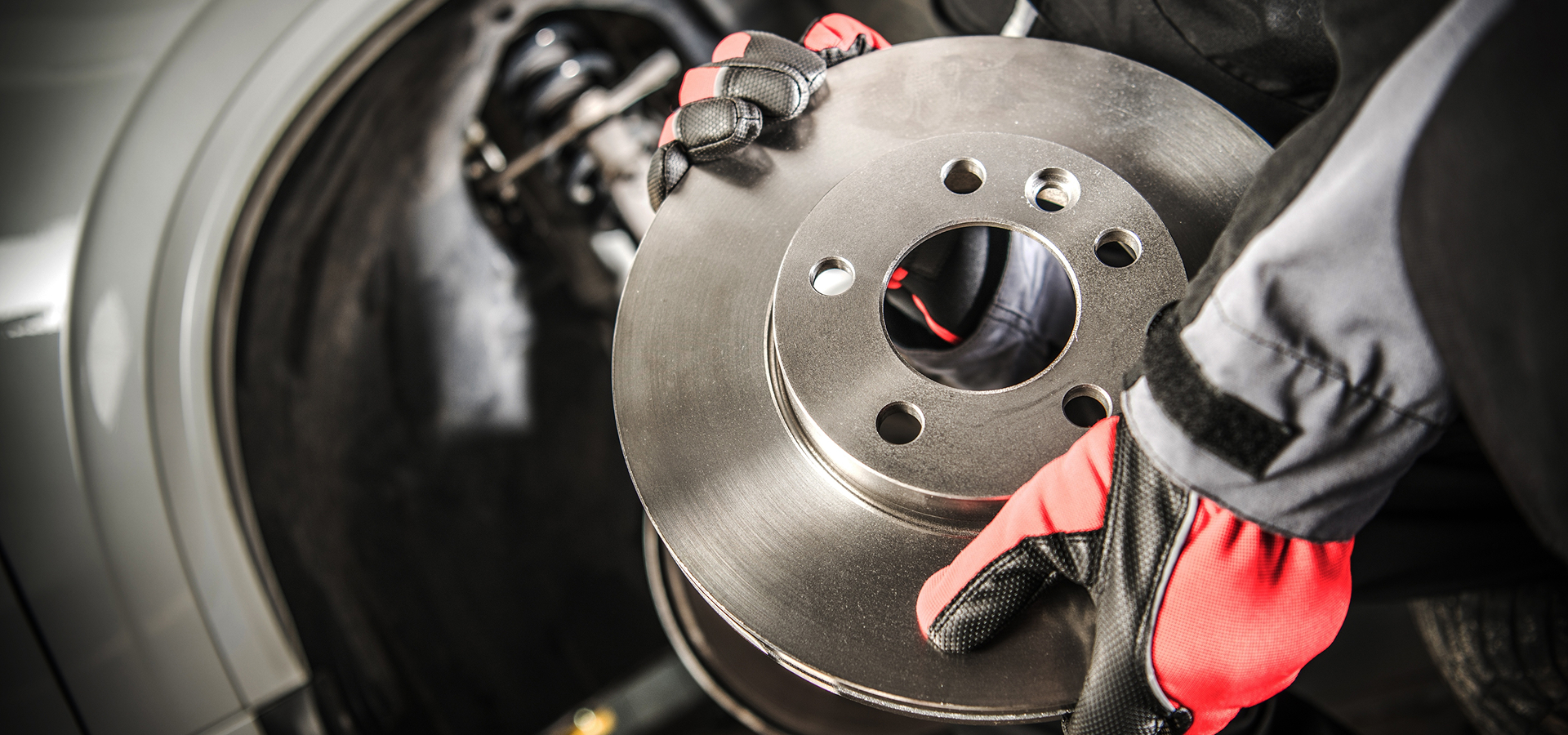 A Telle Tire technician holding a new brake disc while performing repairs on a vehicle.