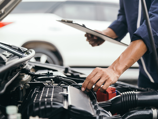 A Telle Tire technician touching an engine component as he holds a clipboard in the opposite hand.