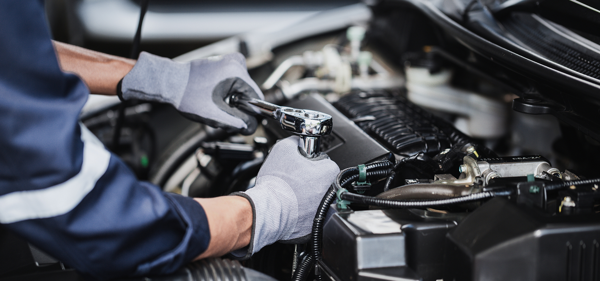 A Telle Tire technician working on a car engine, using a wrench to tighten an engine component.