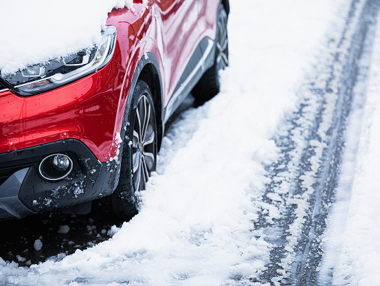 A red vehicle parked along a snow-covered road with snow on the top of the hood.