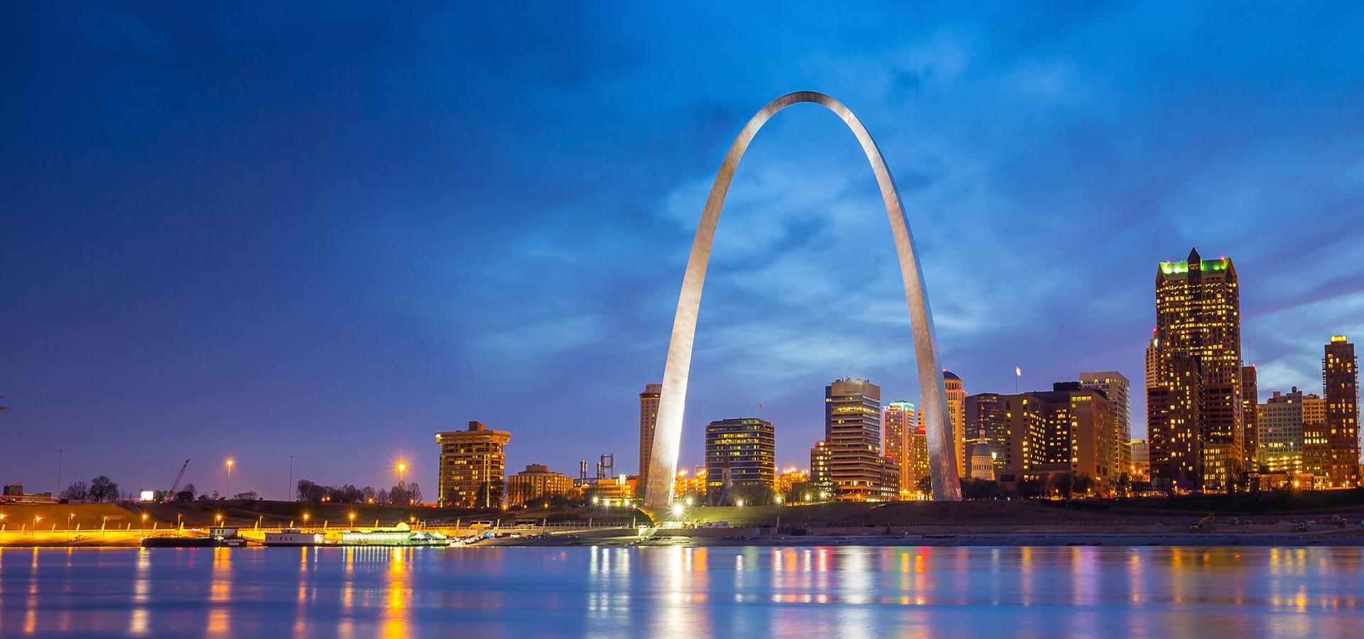 The St. Louis city skyline behind the Gateway Arch, taken from across the river just after sunset.