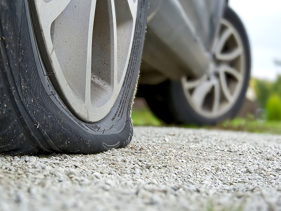 Close up of a flat tire on a vehicle, parked on a small gravel area.