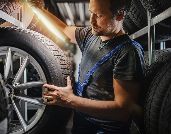 Tire technician closely examining the tread of a new tire with a bright light.