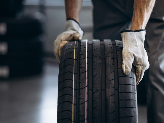 A Telle Tire mechanic wearing gloves and rolling a new tire across the shop.