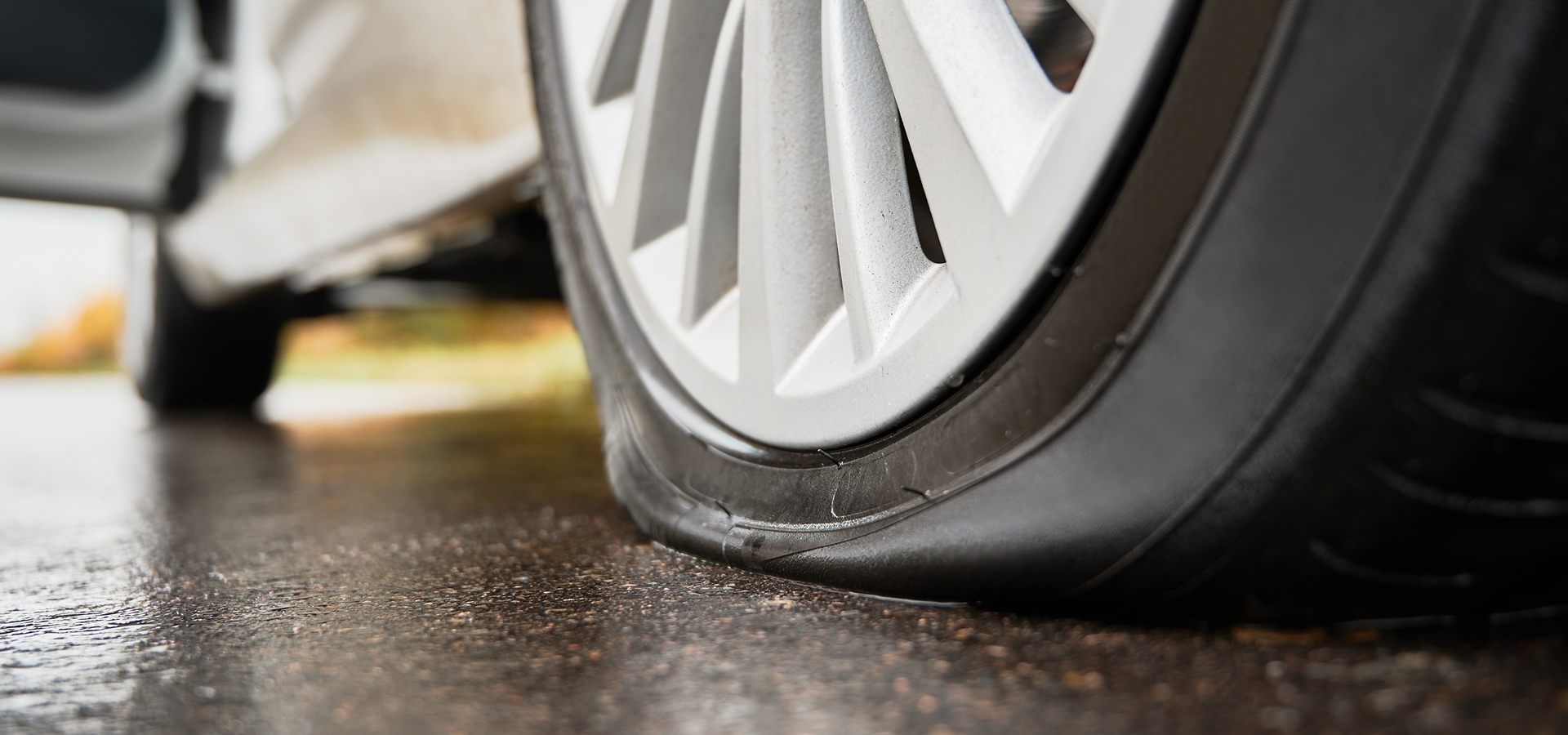 Closeup of a flat tire on a vehicle parked on a slightly wet road surface.