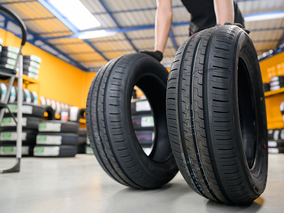 A Telle Tire technician rolling two brand new tires across the shop floor toward the camera.