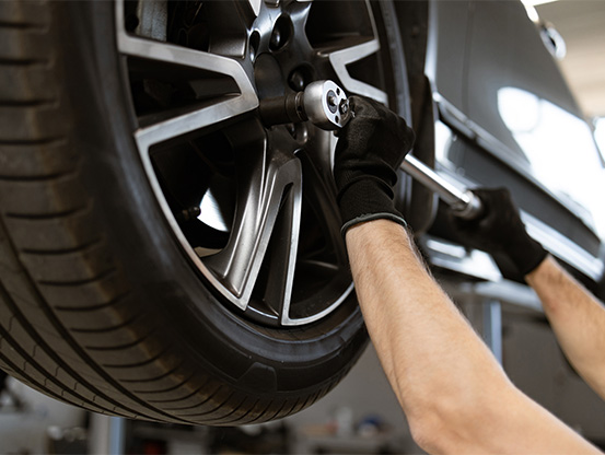 A Telle Tire mechanic tightening the lug nuts on the tire of a vehicle that has been raised on a lift in the shop.