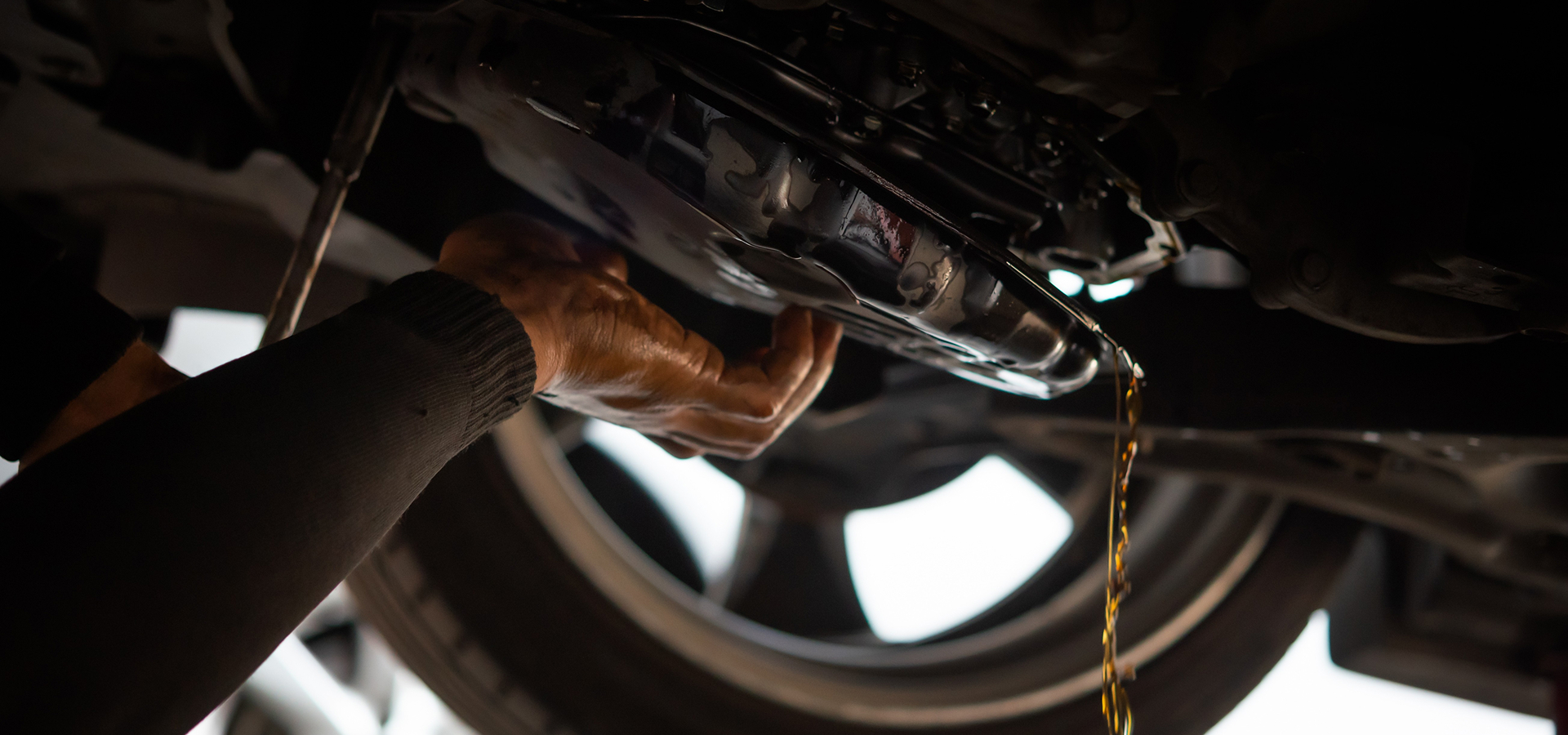 A Telle Tire mechanic draining the old transmission fluid out of the system beneath a vehicle during transmission maintenance.