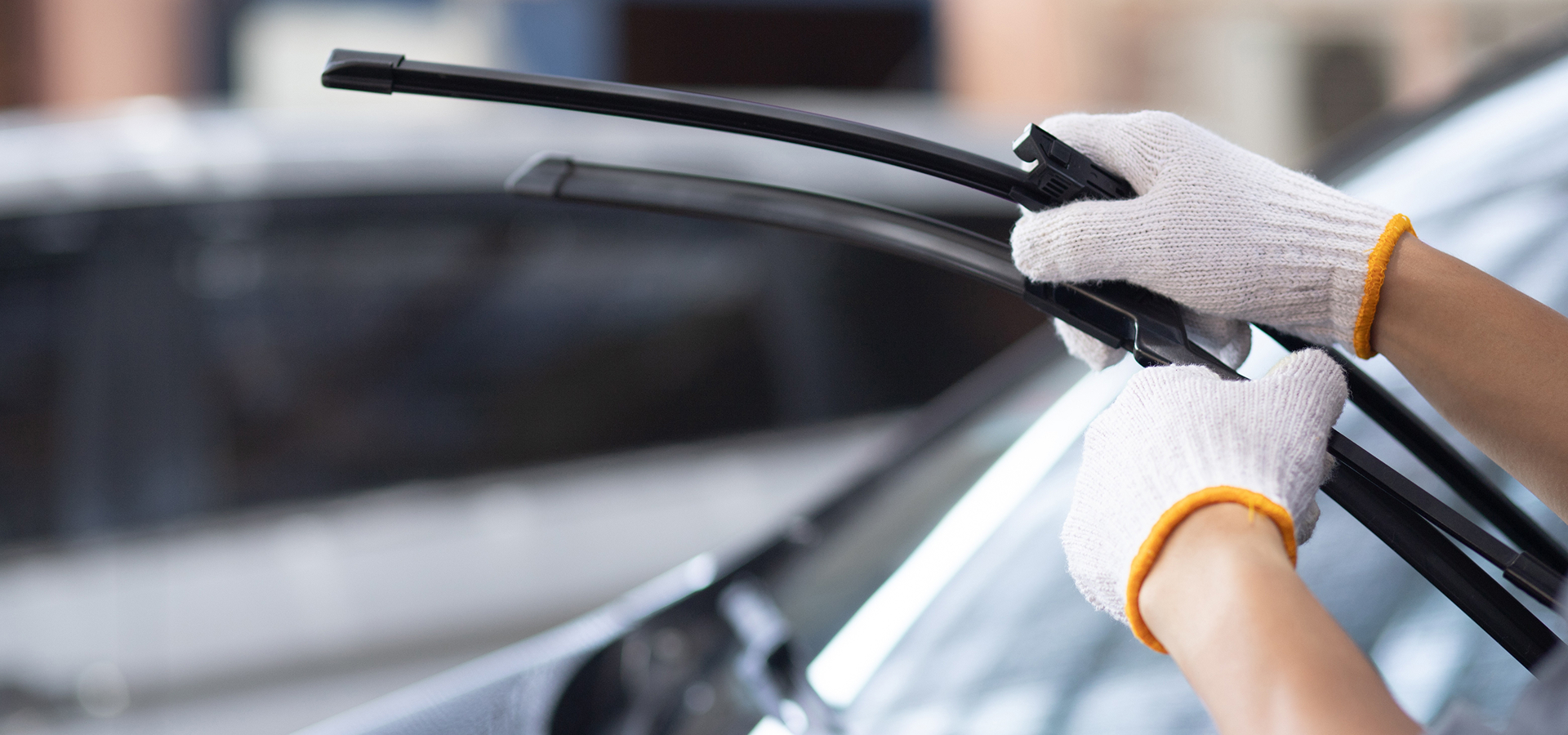 A Telle Tire technician wearing white gloves while replacing the wiper blades on a vehicle for a customer.