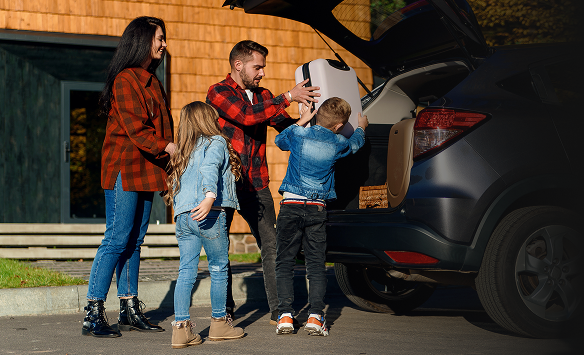 A mother, father, and two young children working together to put luggage into the trunk of their small SUV.