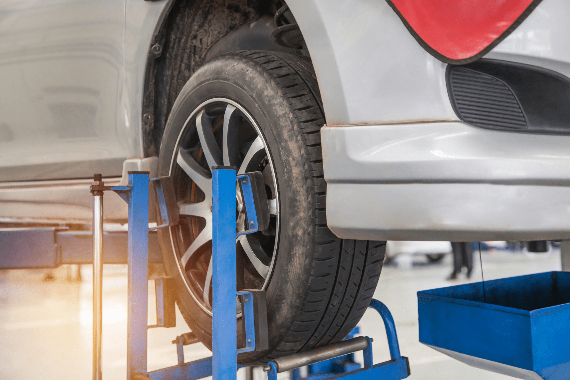 A vehicle lifted up in a shop with a jack holding one of the tires in place.