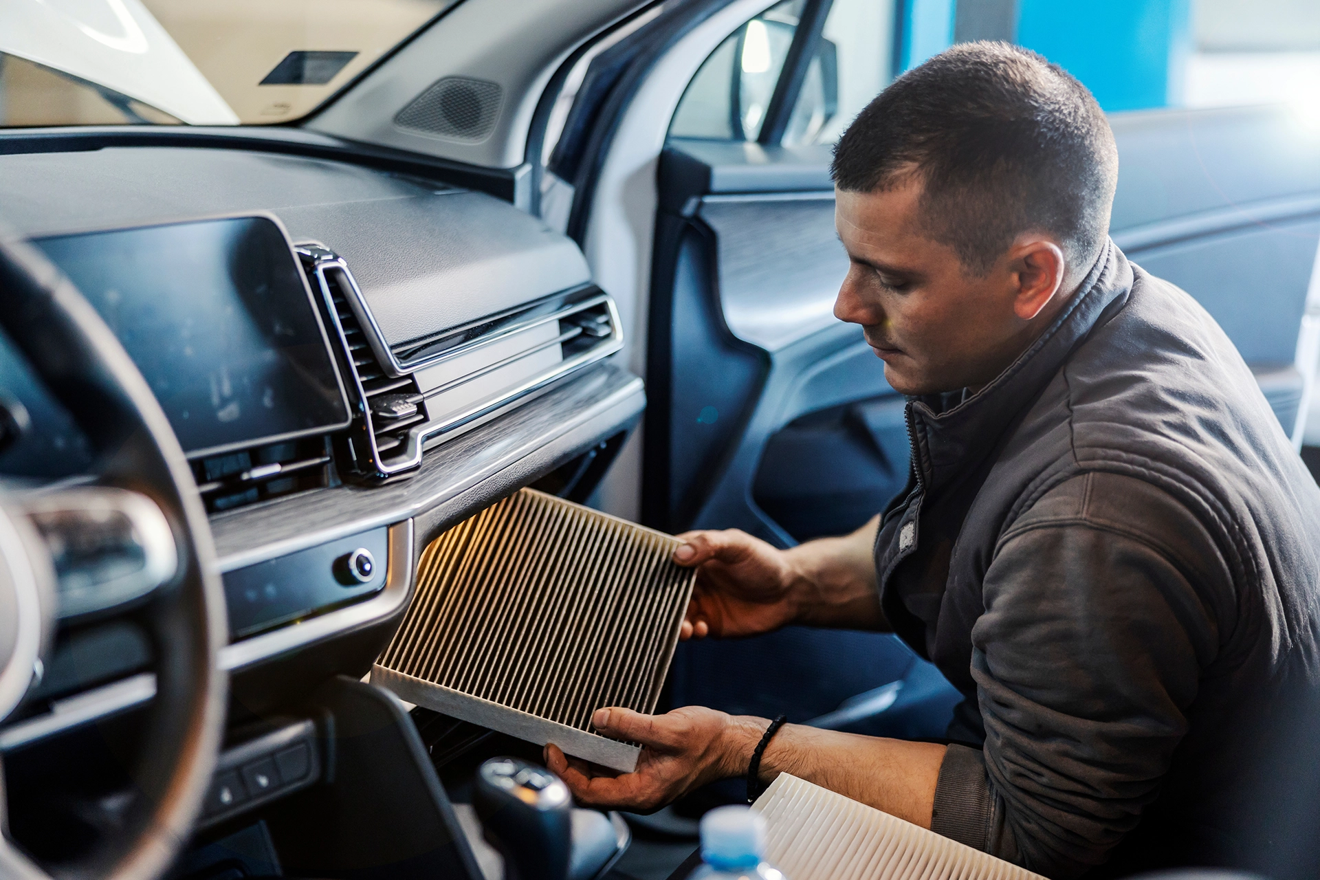 A Telle Tire technician removing the cabin air filter from the glovebox area of a vehicle for inspection.