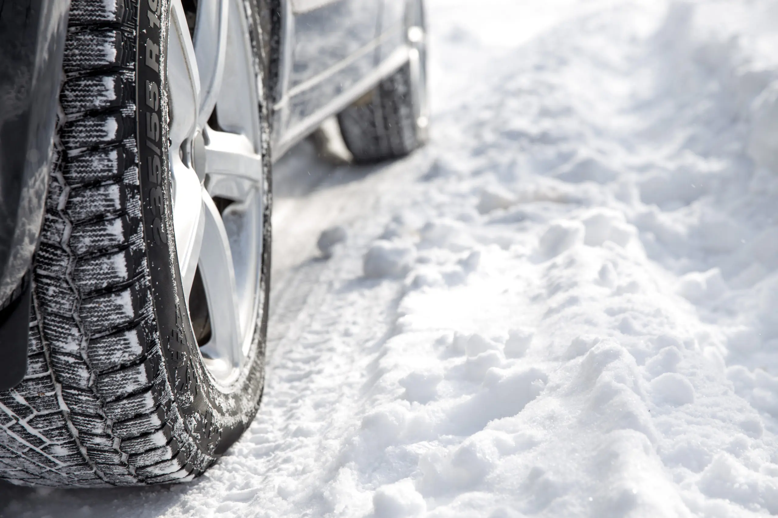 Close up of snow-filled tire treads on the tires of a vehicle driving on a snow-covered road.