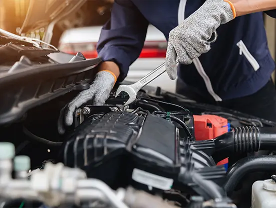 A Telle Tire mechanic wearing gloves while using a wrench on a component inside a vehicle's engine.