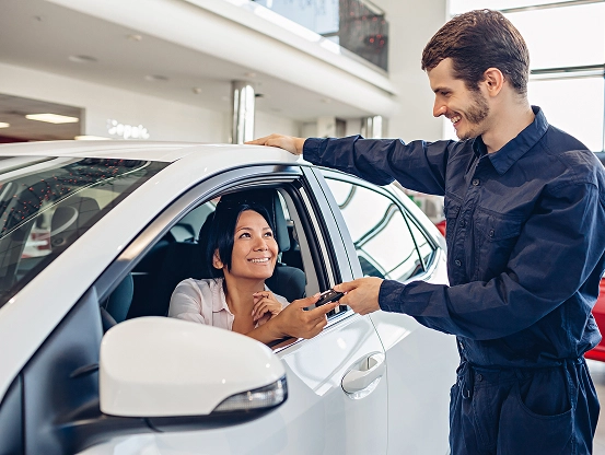 A Telle Tire service expert smiling and handing the car keys back to a smiling customer seated in her car.